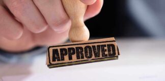 A hand holding a wooden stamp with the word 'APPROVED' above a document