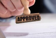 A hand holding a wooden stamp with the word 'APPROVED' above a document