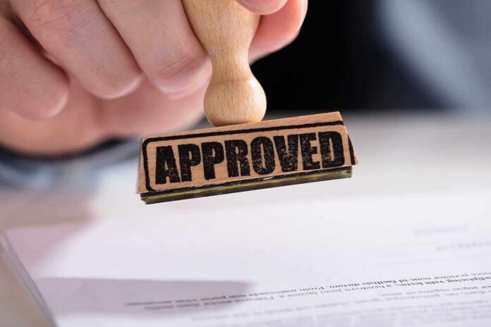 A hand holding a wooden stamp with the word 'APPROVED' above a document