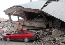 A red car parked next to a collapsed building with debris scattered around
