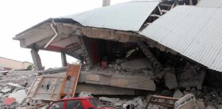 A red car parked next to a collapsed building with debris scattered around
