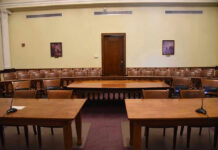 Empty courtroom with wooden tables, chairs, and a door.