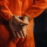 Person in orange jumpsuit with handcuffs behind back.