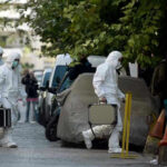 Investigators in hazmat suits carrying equipment cases.