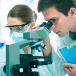 Miracle Nasal Spray Halts Brain Aging? Two scientists conducting an experiment in a laboratory, one looking through a microscope and the other holding a flask with blue liquid