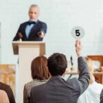 Mystery Bidder Drops $9M for LUNCH! Auctioneer at podium as bidder raises numbered paddle