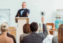 Auctioneer at podium as bidder raises numbered paddle