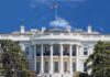 The White House with the American flag flying against a blue sky