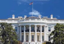 The White House with the American flag flying against a blue sky