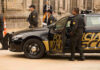 Police officers standing and sitting near a patrol car.