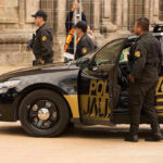 Police officers standing and sitting near a patrol car.