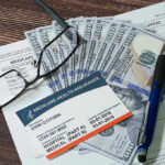 Medicare card glasses pen money on wooden table