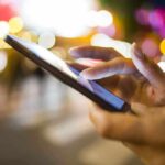 A persons hand using a smartphone in a city at night with blurred lights in the background