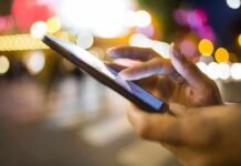 Phone Chase Turns Deadly A persons hand using a smartphone in a city at night with blurred lights in the background