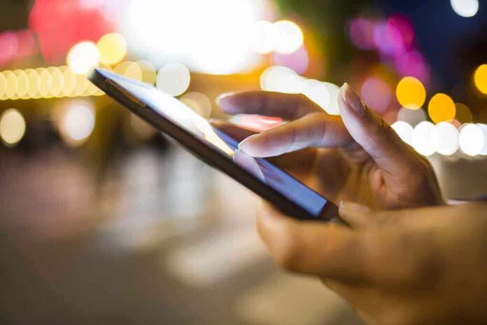 shutterstock_160559990 A persons hand using a smartphone in a city at night with blurred lights in the background