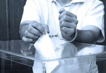Funding Hammer Drops — Paper Ballots Now A handcuffed individual placing a ballot into a transparent voting box