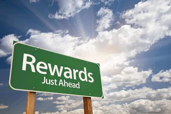 shutterstock_79429900-1 A green road sign indicating rewards just ahead against a cloudy sky