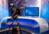 Live TV Took A Wild Turn TV studio with camera and empty anchor desk.