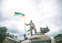 Russia Burns Through Men and Machines Soldier on tank holding Ukrainian flag.