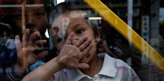 A child playfully covering their face while looking through a glass window