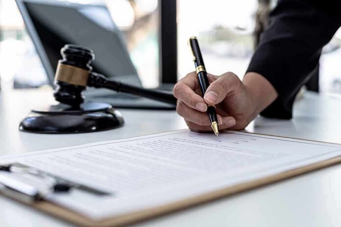 Hand signing legal document beside gavel and laptop