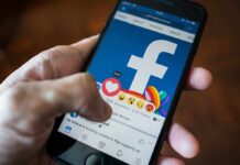 Hand using smartphone with Facebook reactions on screen