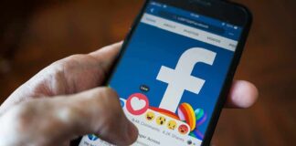 Hand using smartphone with Facebook reactions on screen