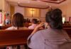 people seated in church pews facing a cross