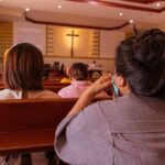 people seated in church pews facing a cross
