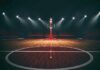 Basketball hoop on an empty indoor court under bright arena lights