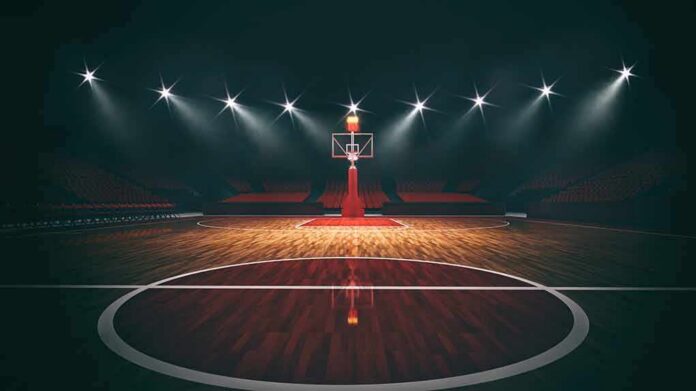 Basketball hoop on an empty indoor court under bright arena lights