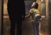 Girl with backpack holding hands with adult in an elevator