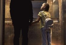 Girl with backpack holding hands with adult in an elevator