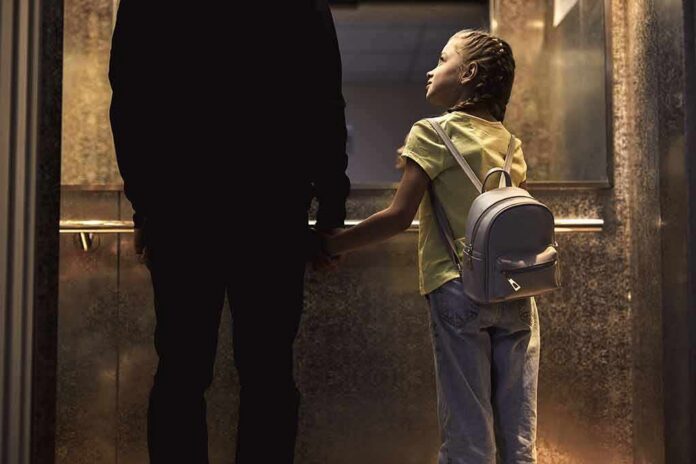 Girl with backpack holding hands with adult in an elevator