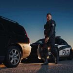 Police officer standing near patrol car during twilight traffic stop