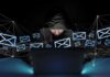 Hooded person using a laptop surrounded by email icons