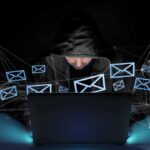 Hooded person using a laptop surrounded by email icons