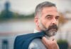 Man with gray beard holding a jacket over his shoulder