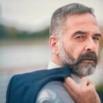 Man with gray beard holding a jacket over his shoulder