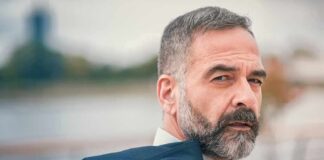 Man with gray beard holding a jacket over his shoulder