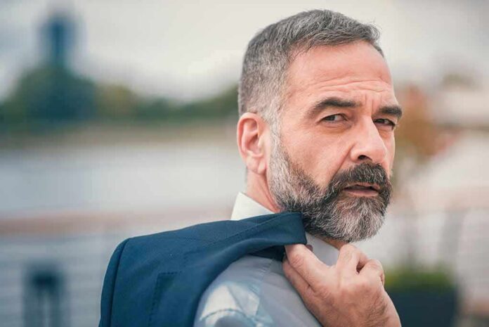 Man with gray beard holding a jacket over his shoulder