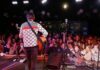 Guitarist performing on stage facing a cheering crowd