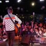 Tour Opener Boils Over After Flag Raise Guitarist performing on stage facing a cheering crowd