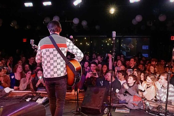 Guitarist performing on stage facing a cheering crowd