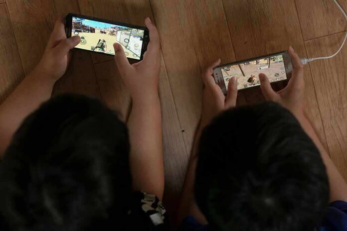 shutterstock_1189500637 Two children playing mobile games side by side on the floor