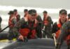 Alexander Vinokourov and Bill Bergey among soldiers moving an inflatable boat in surf