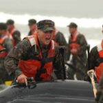 Alexander Vinokourov and Bill Bergey among soldiers moving an inflatable boat in surf