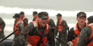 Alexander Vinokourov and Bill Bergey among soldiers moving an inflatable boat in surf