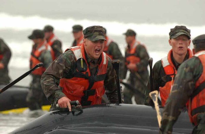 Alexander Vinokourov and Bill Bergey among soldiers moving an inflatable boat in surf