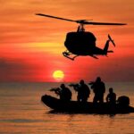 Helicopter hovers above armed team in inflatable boat at sunset